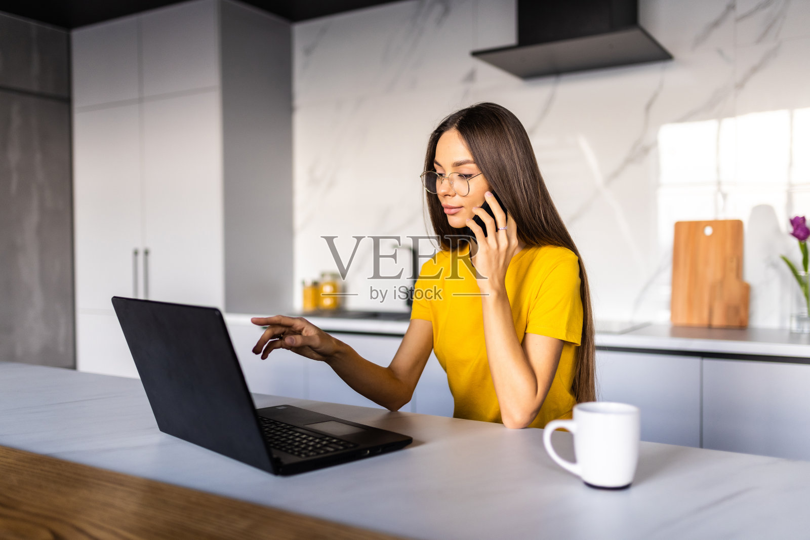 年轻女子使用笔记本电脑蚂蚁打电话,而花时间在厨房照片摄影图片