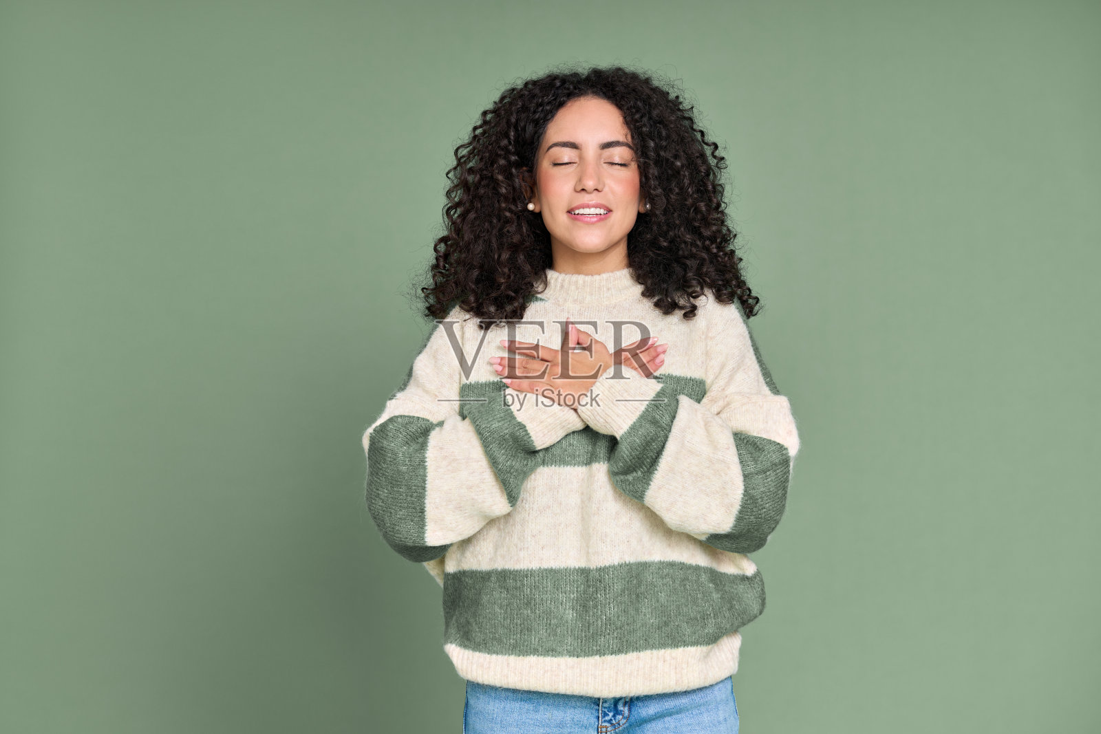 年轻平静快乐的拉丁女子在胸前牵着手孤立的绿色。照片摄影图片