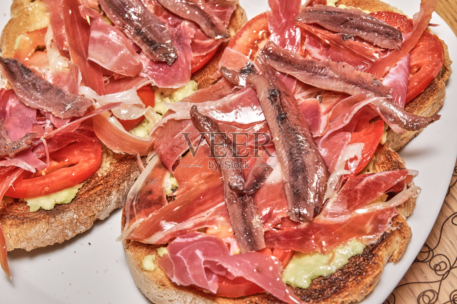 酥脆的吐司上撒着美味的伊比利亚火腿、多汁的番茄片、奶油鳄梨,再淋上一点初榨橄榄油来提味。一个完美的组合,以满足味蕾。照片摄影图片