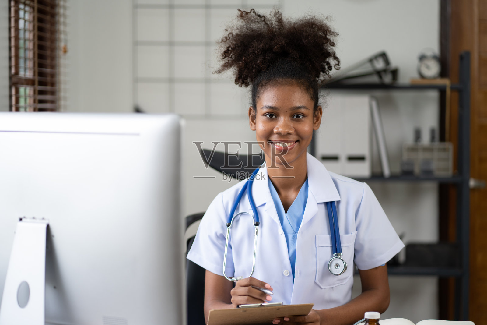 女非裔美国医生坐在诊所的办公室里。使用台式电脑工作。照片摄影图片