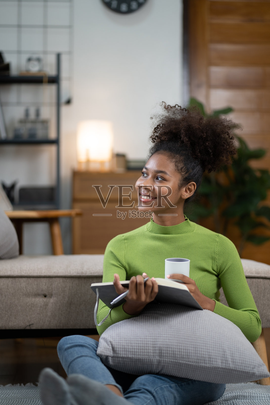 年轻的非裔美国妇女在家里的沙发上喝茶看书。照片摄影图片