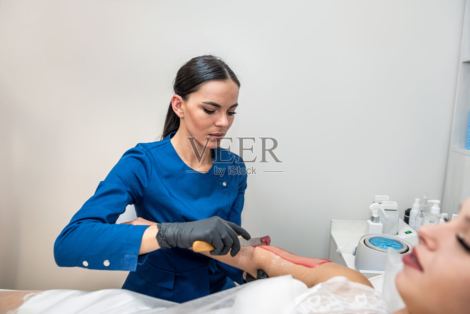 美容院美容师用热糖给女顾客打蜡。照片摄影图片