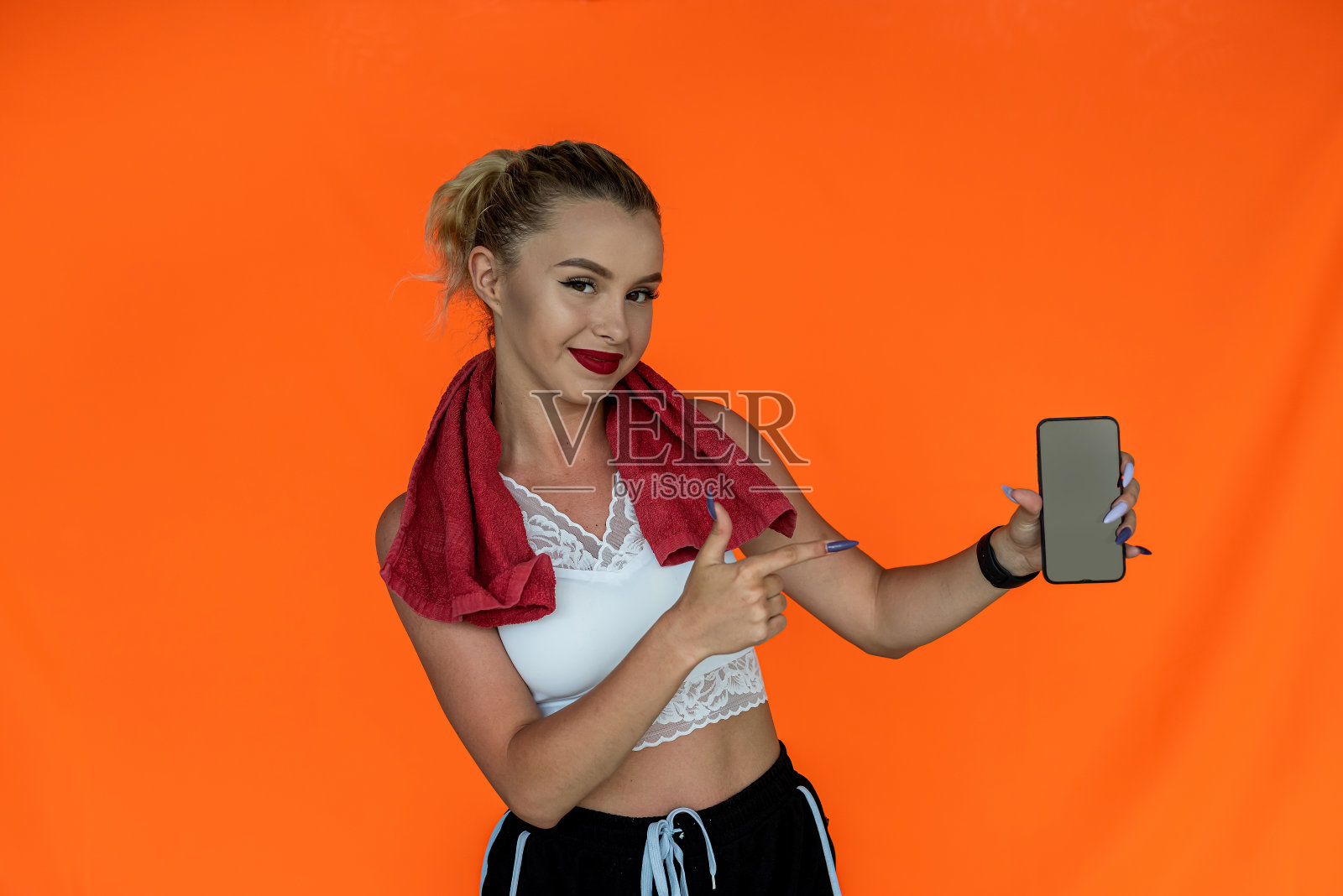 迷人的性感年轻女子摆姿势与食指指向手机上的色彩工作室照片摄影图片