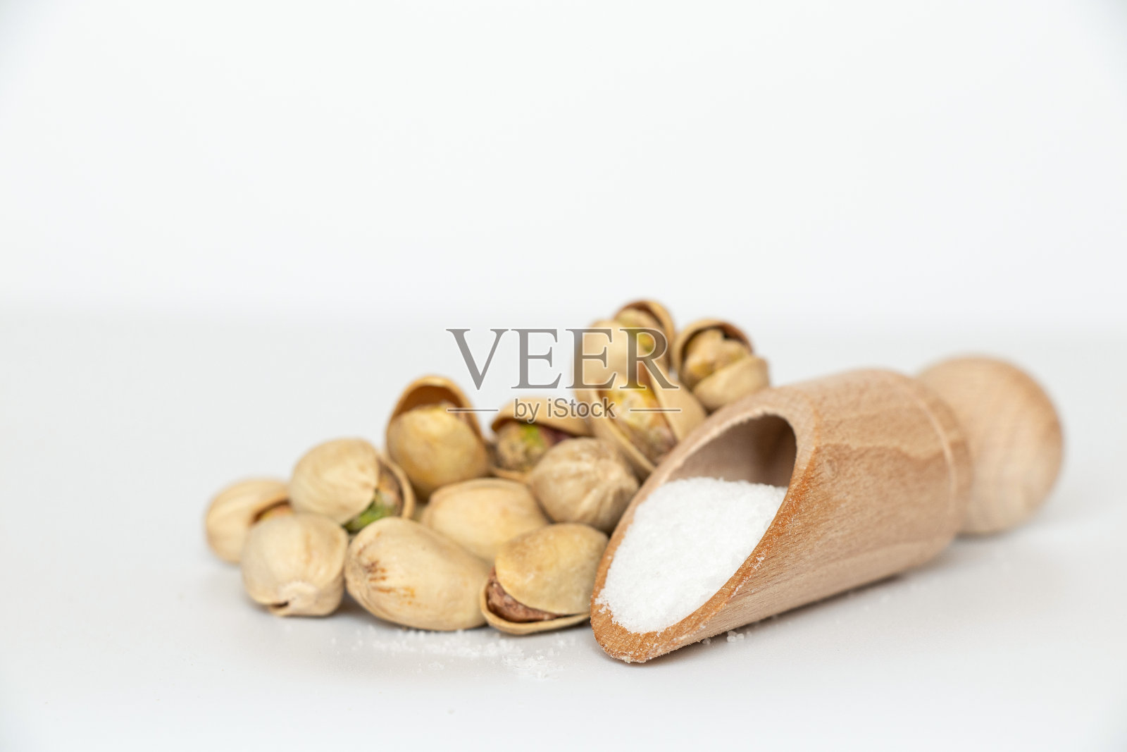 一串开心果和白底撒盐的木勺照片摄影图片