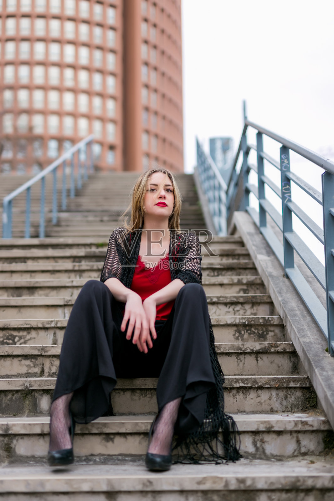 年轻漂亮的金发女人坐在城市的楼梯上照片摄影图片