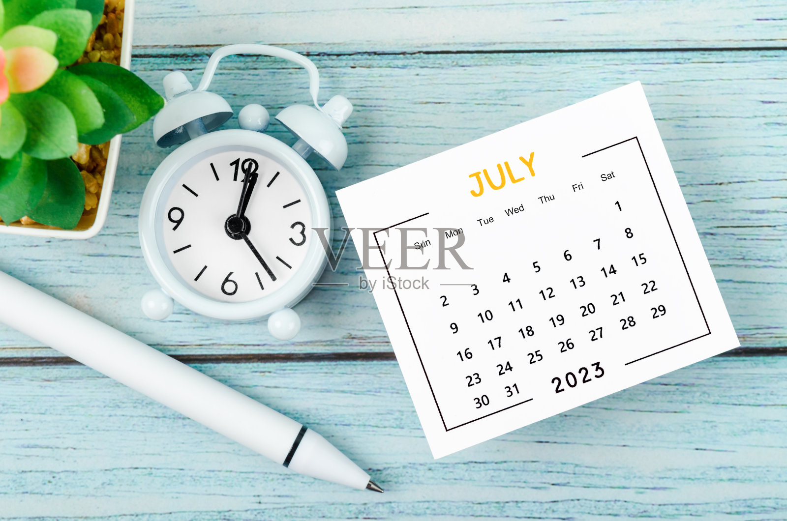 2023年7月日历年和闹钟,蓝色木制背景上的钢笔。照片摄影图片