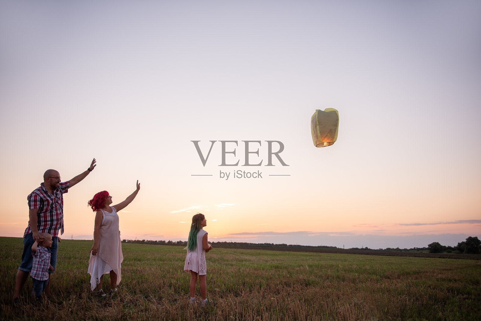 希望的概念。团队合作。多样性家庭在日落时分在野外发射黄色的天灯。照片摄影图片