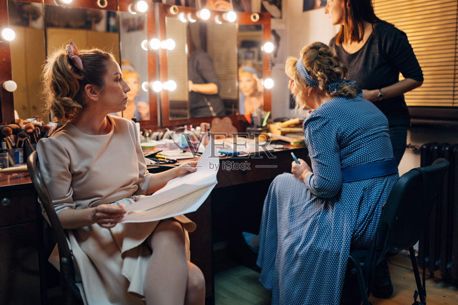 一位化妆师为一位资深女演员化妆,另一位女演员坐在她们旁边排练剧本照片摄影图片
