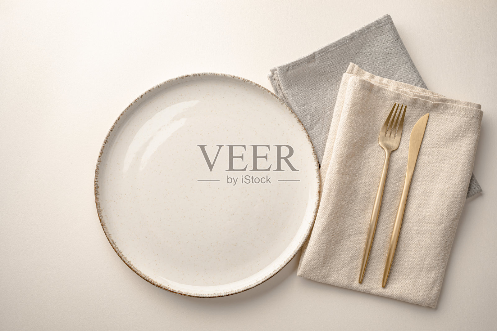 空的奶油色盘子,亚麻餐巾和金色餐具放在桌上。照片摄影图片