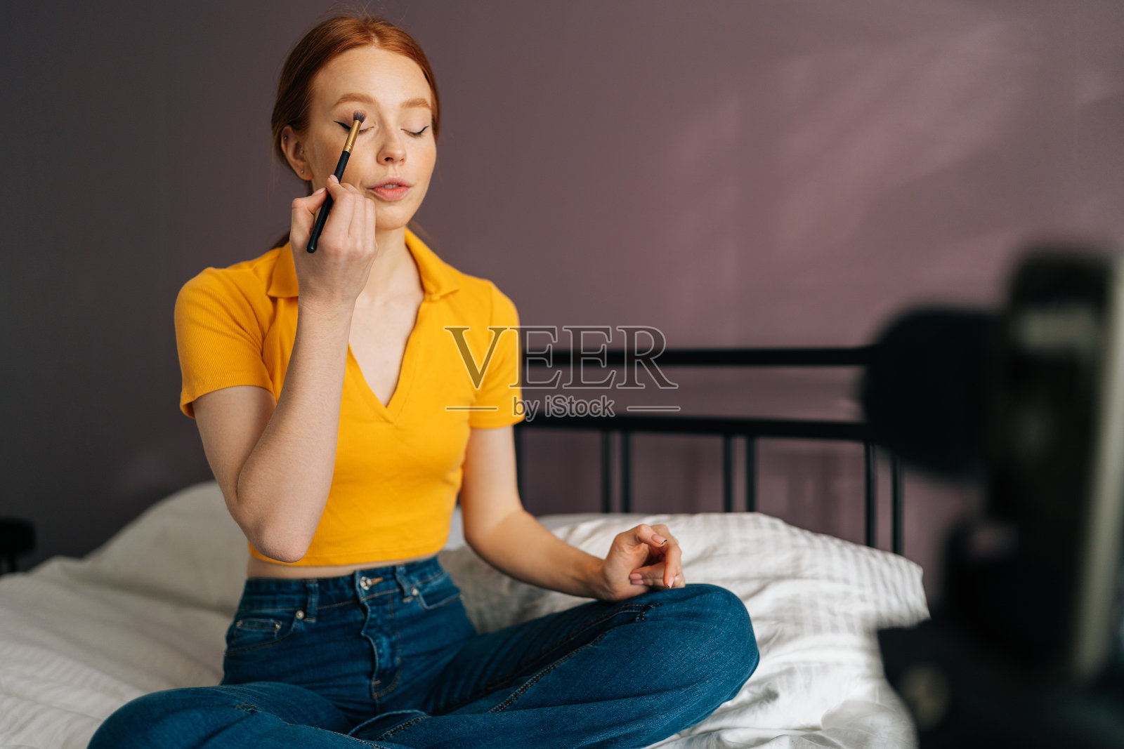 红发美妆女博主,用专业相机站在三脚架上录制化妆品评测、眼影、频道视频。照片摄影图片