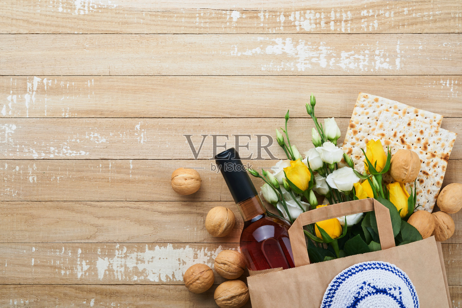 逾越节庆祝概念。无酵饼,犹太红酒,核桃,白玫瑰和黄玫瑰。传统仪式犹太面包上的沙色旧瓦墙背景。逾越节是犹太人的节日。俯视图照片摄影图片