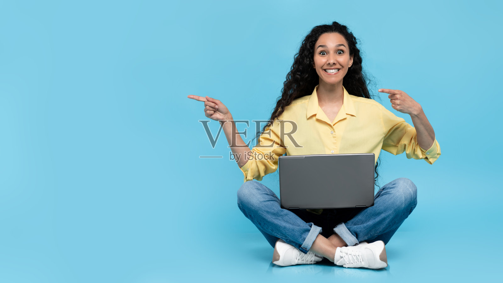 快乐的年轻女士使用笔记本电脑进行在线工作、教育或交流,并指向空白处照片摄影图片