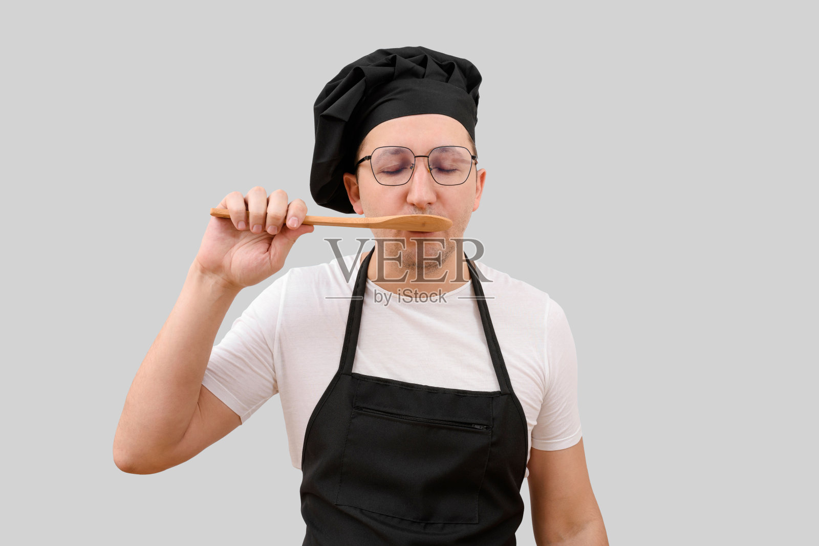 孤立在灰色背景中的厨师用勺子品尝食物。烹饪和人的概念照片摄影图片