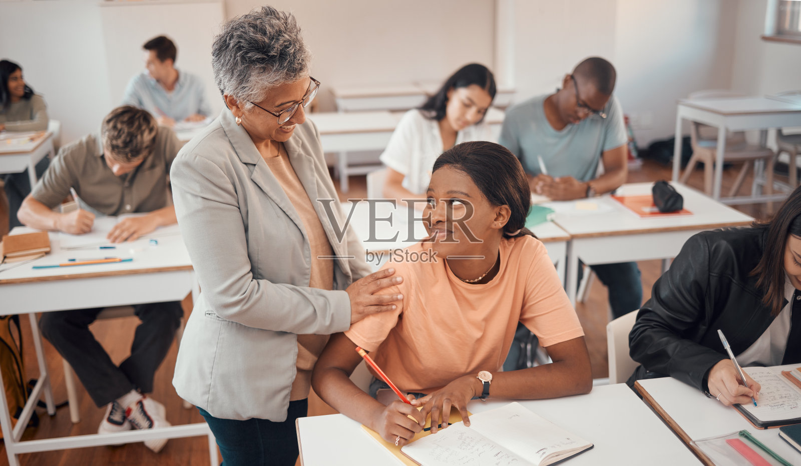 老师,学生,考试的教室,高等教育的知识和学习。年轻女性,黑人女性或教育工作者帮助学生考试,谈话或学生在书上或焦点上写笔记照片摄影图片