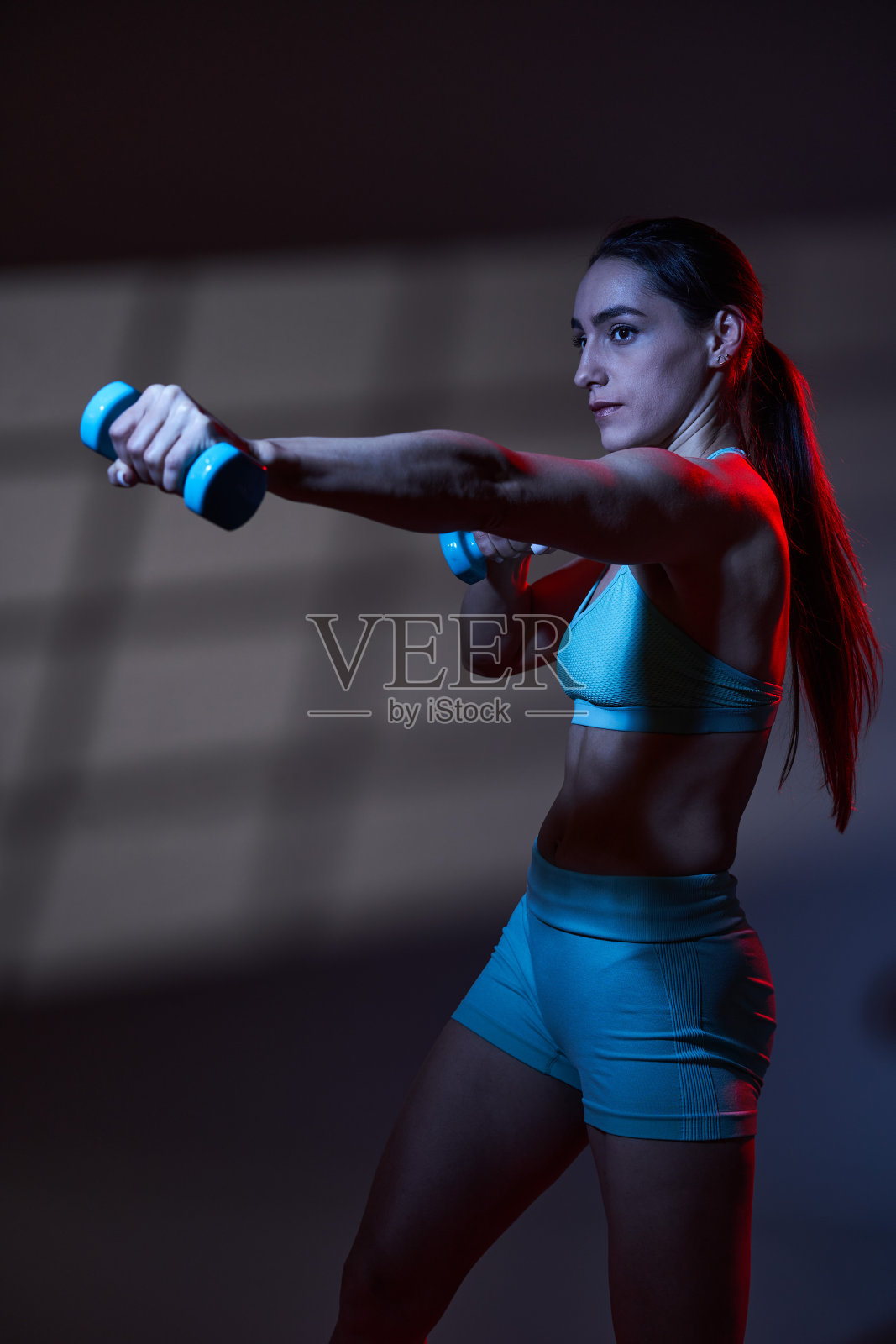 健身女模特与伟大的身体在红蓝色的强光下工作照片摄影图片