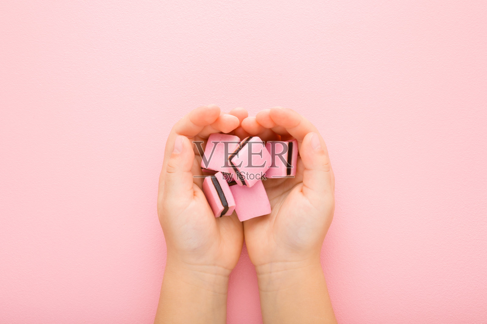 在浅粉色的桌子背景上,小女孩张开的手掌上有黑巧克力果冻软糖。柔和的颜色。甜的零食。特写镜头。视角镜头。自顶向下视图。照片摄影图片