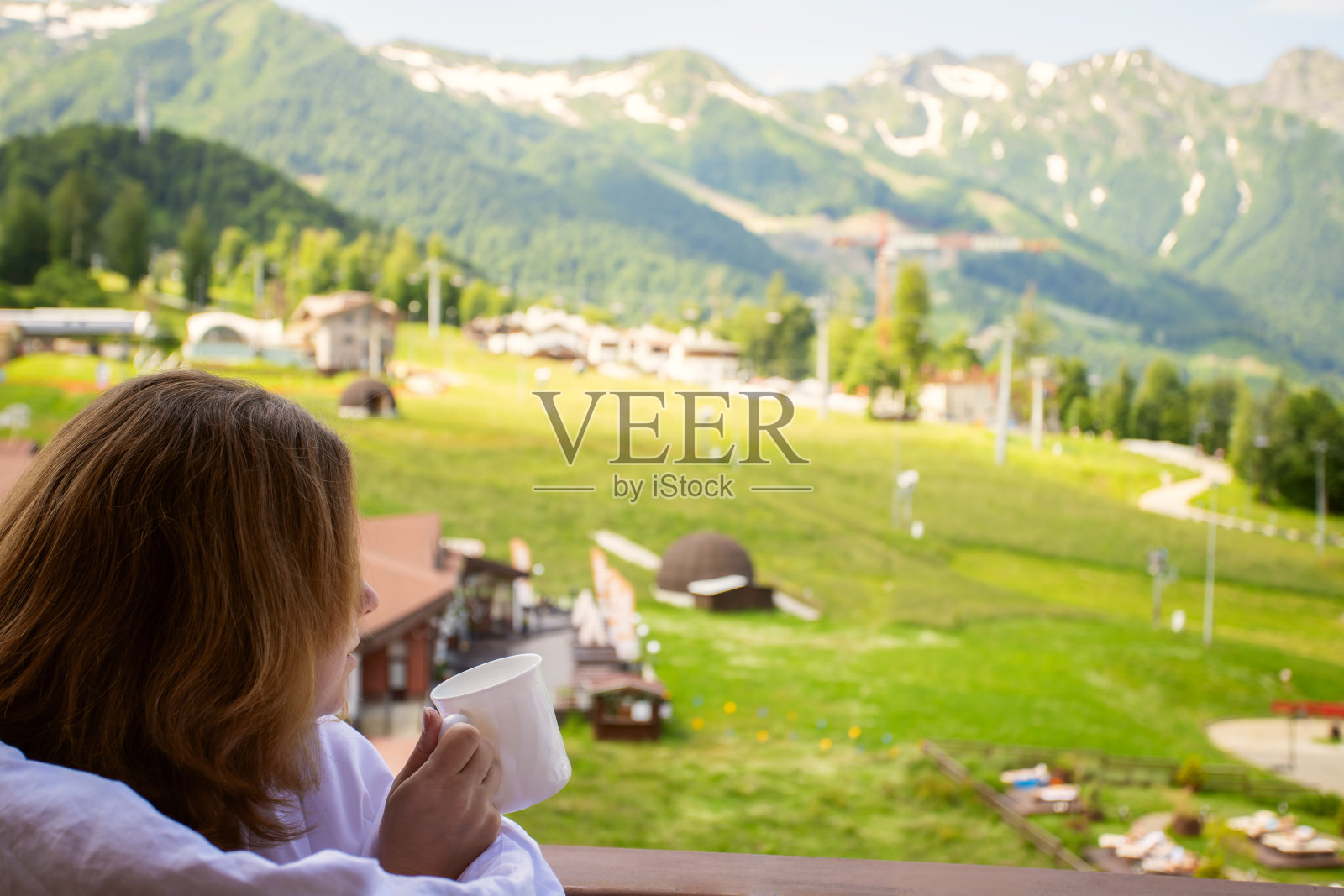 生态酒店,健康和水疗中心,阳台上一个女人裹着毯子,端着咖啡,俯瞰着群山照片摄影图片