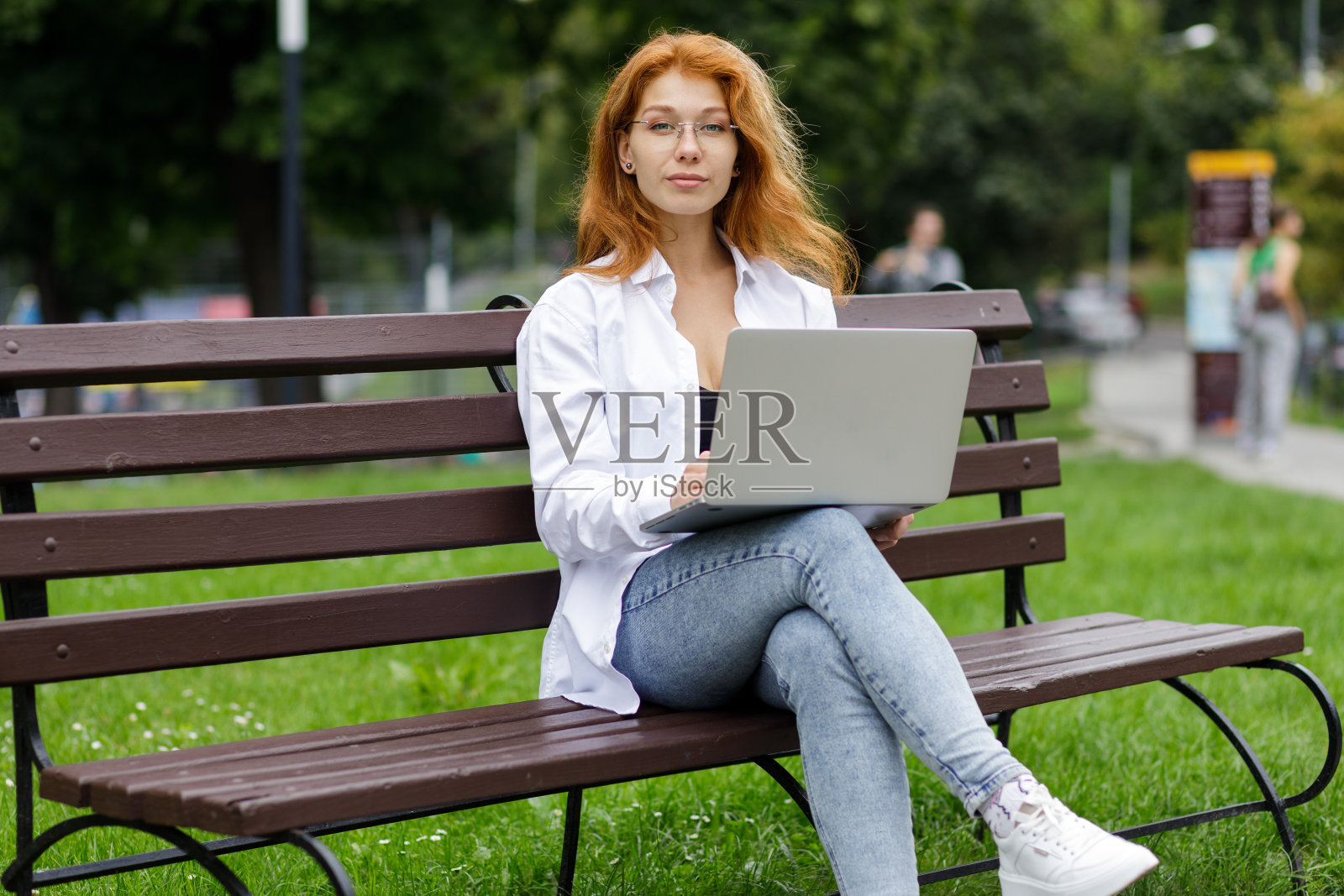 年轻自信有吸引力的学生女孩使用她的笔记本电脑坐在公园的长椅上照片摄影图片