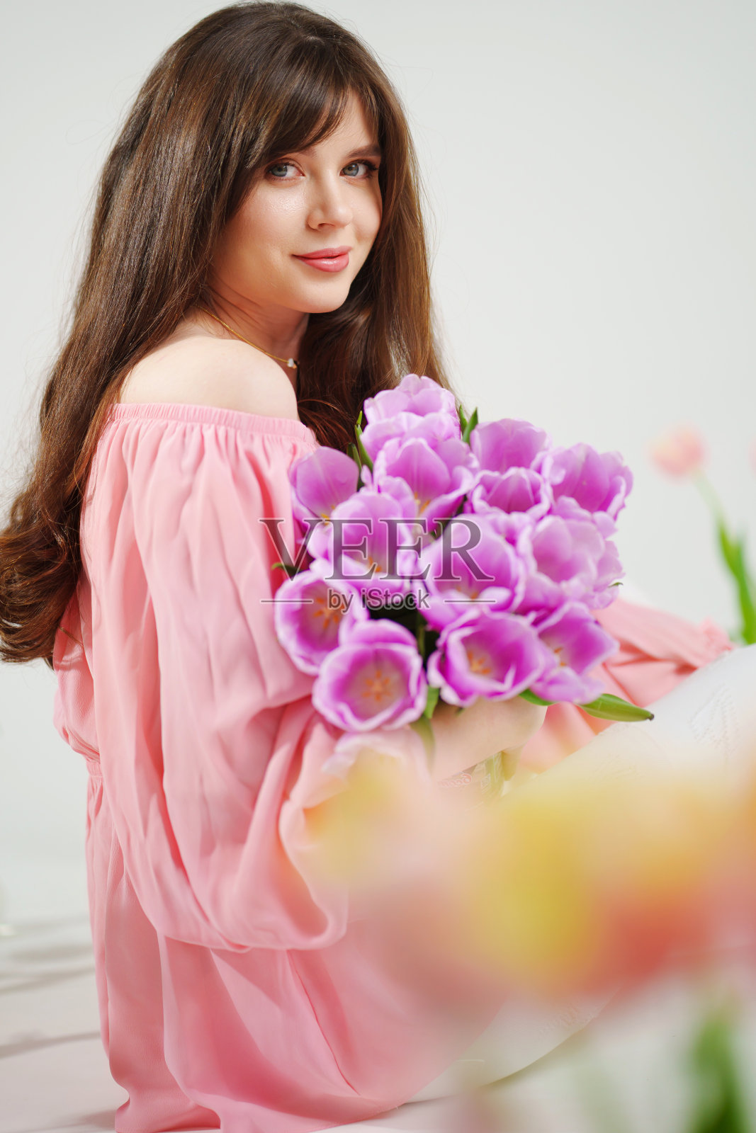 美丽的年轻黑发女人长头发在粉红色和一束郁金香。照片摄影图片