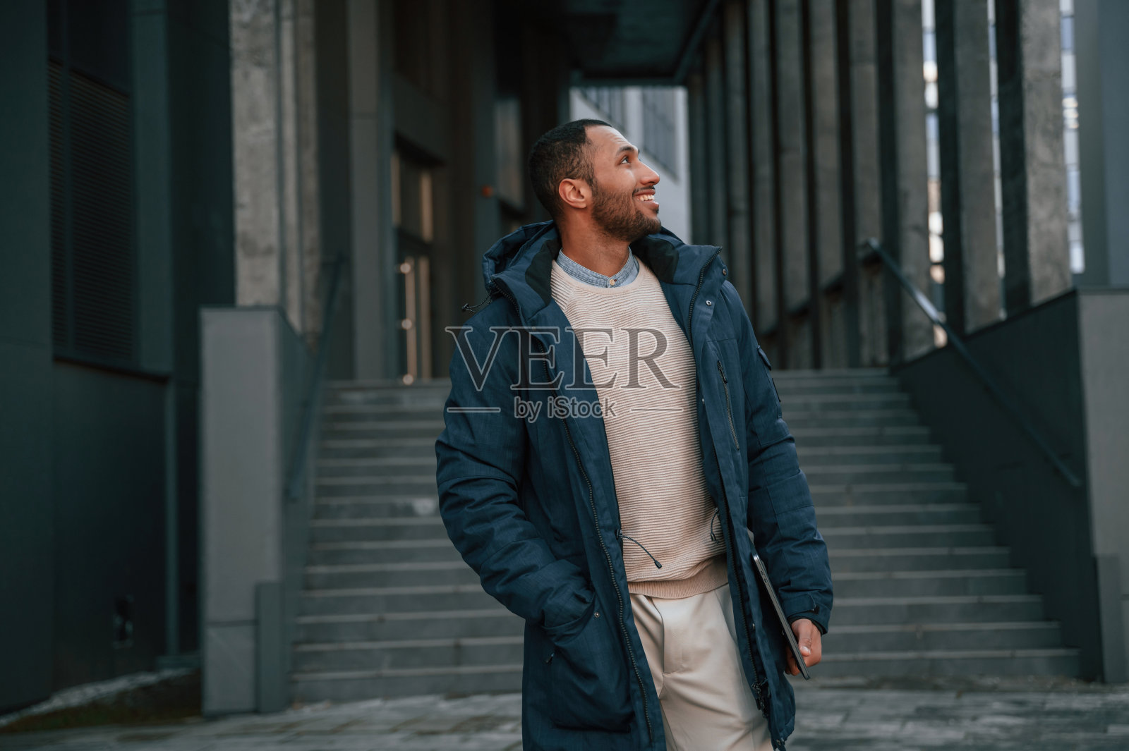 穿着蓝色夹克,手里拿着笔记本电脑。英俊的黑人男子在商业大楼附近的户外照片摄影图片