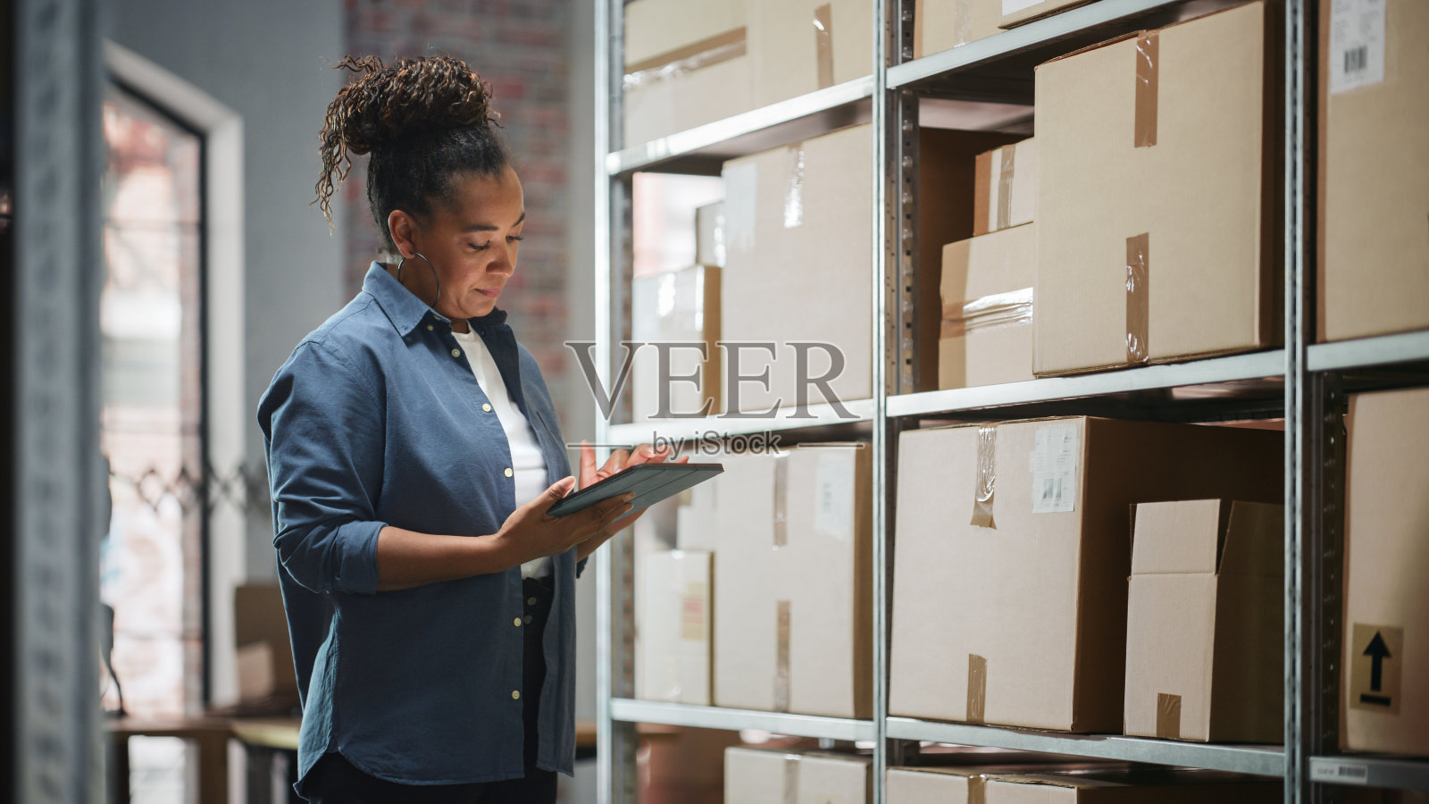 一个成功员工的肖像检查库存,在平板电脑上写作。一名黑人妇女在仓库储藏室里摆姿势拍照,微笑着准备发货的订单。照片摄影图片