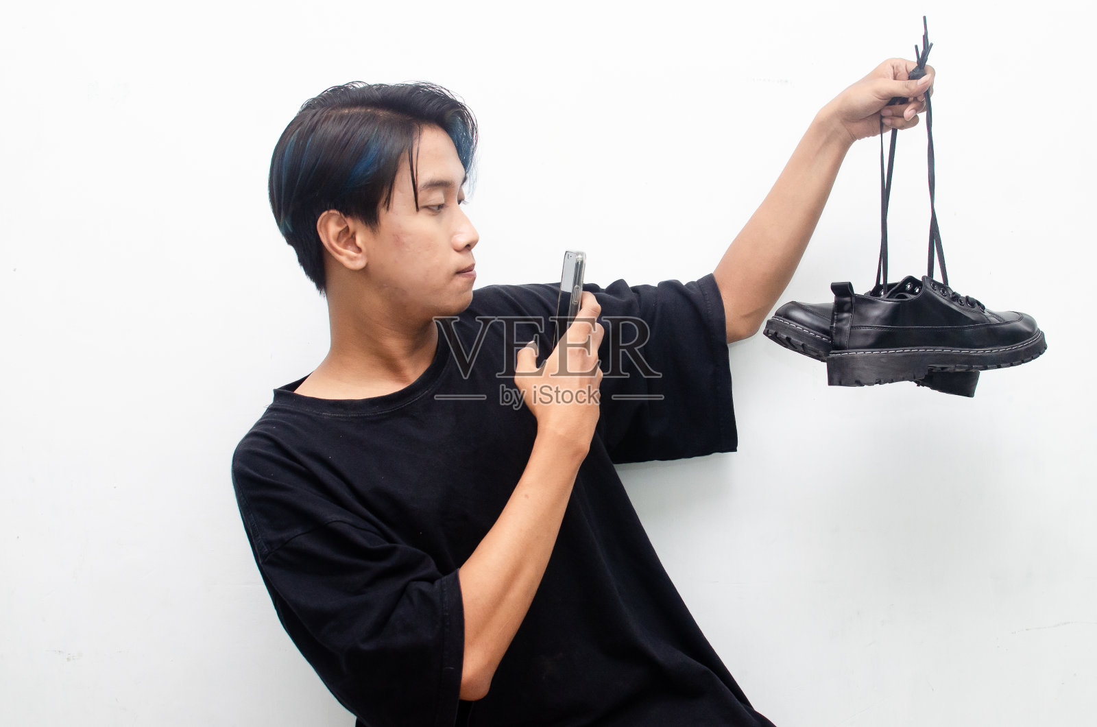 在家购物的概念。一个网上购物的概念,亚洲男人拿着手机和鞋子,快乐的表情被红色隔离。在电子商务中买卖东西的人照片摄影图片