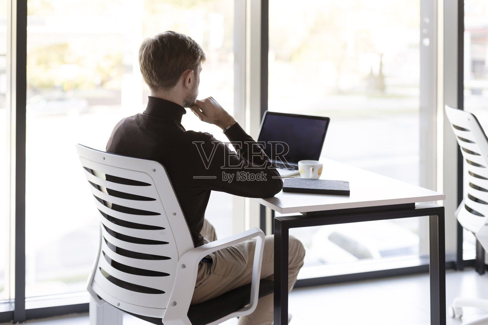 沉思的人坐在办公室的桌子上,在笔记本电脑上工作,背影,现代的工作场所照片摄影图片