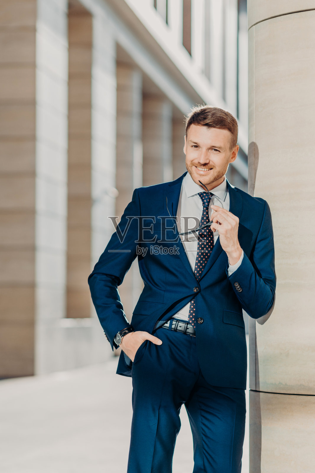 体贴开朗的大胡子男企业家有着令人愉快的笑容,穿着黑色西装,戴着墨镜,在室内摆姿势,为成功的商务会议和与合作伙伴签订合同而高兴照片摄影图片