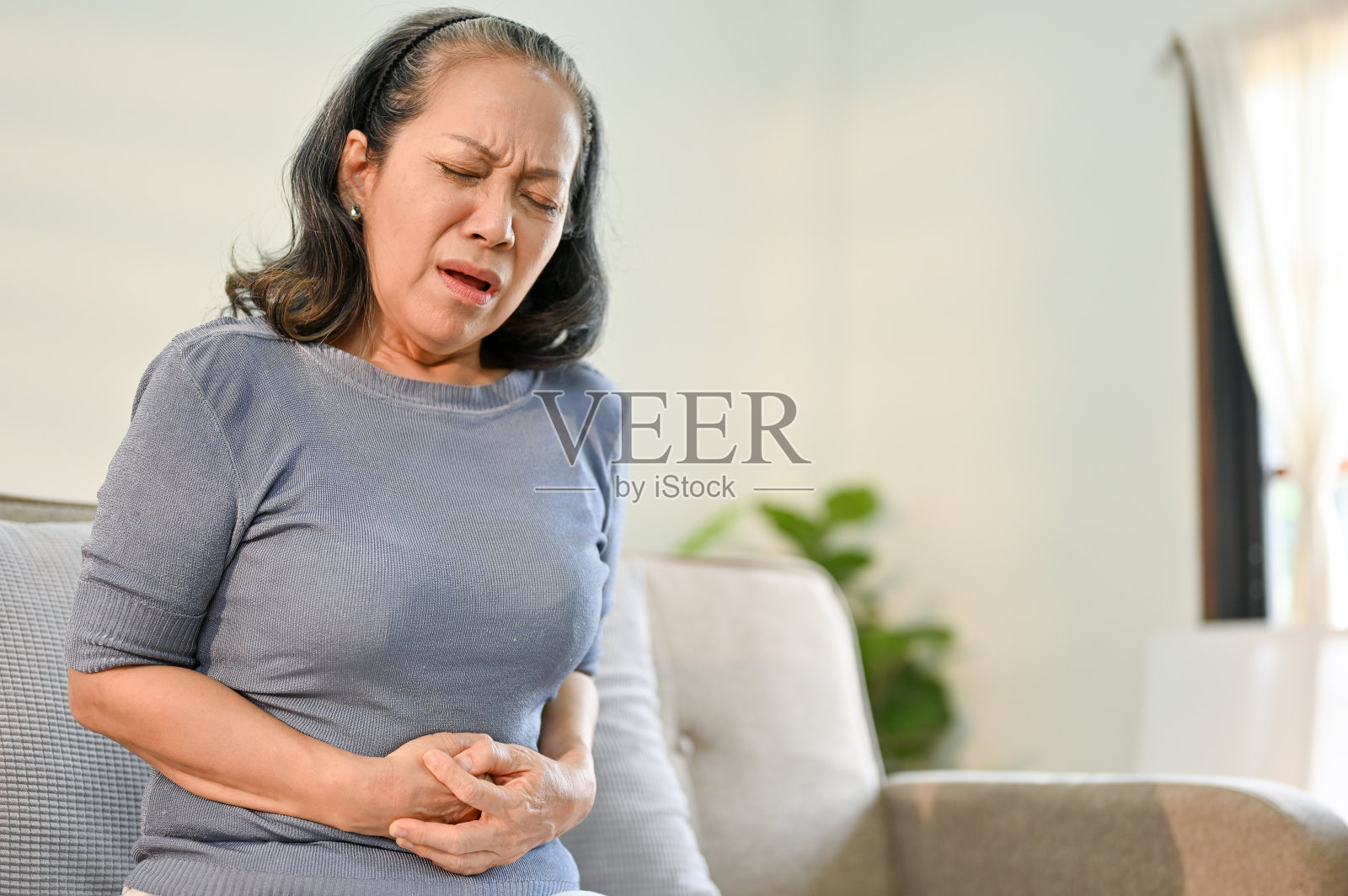 生病的亚洲老妇人肚子痛,摸着肚子有疼痛的感觉照片摄影图片