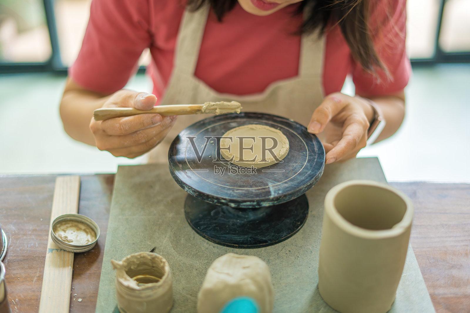 俯视图女陶工在制陶车间用陶土制作陶罐。专注手年轻女子将粘土产品部分连接到未来的陶瓷产品。陶器作坊。照片摄影图片