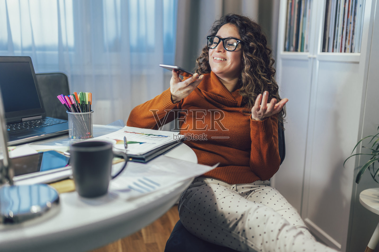 年轻女子使用手机工作,在家里打语音电话。照片摄影图片