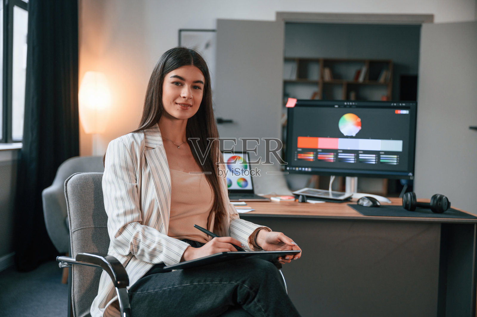 坐在椅子上。设计师的软件在屏幕上。女人在有电脑的现代化办公室里工作照片摄影图片