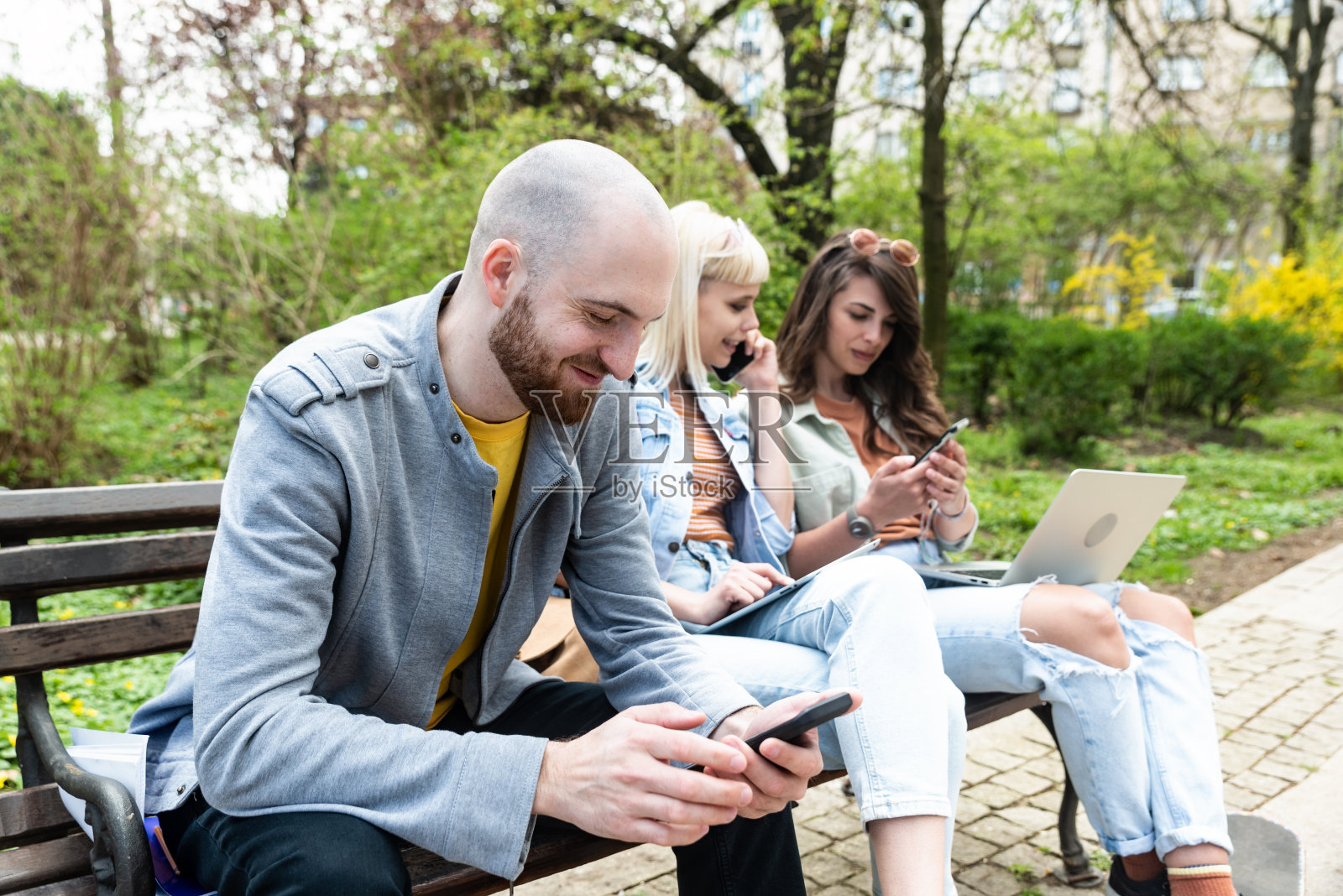 为了把小公司搬到办公室,年轻的企业家们正在公园里的长椅上举行职员会议,寻找出租的场地或公寓。年轻热情的专家们正在寻找公寓。照片摄影图片