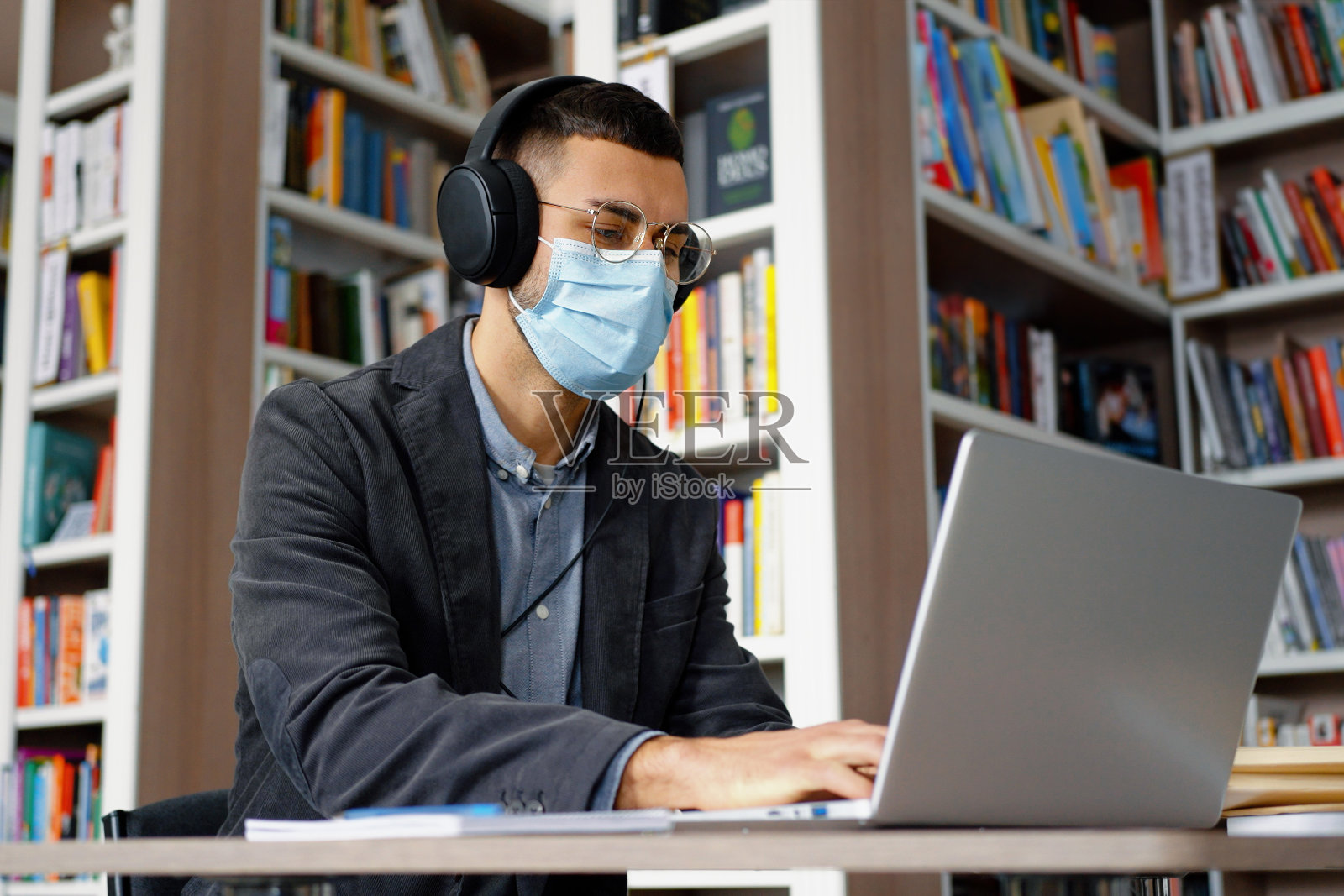戴面具的男子在图书馆用笔记本电脑工作照片摄影图片
