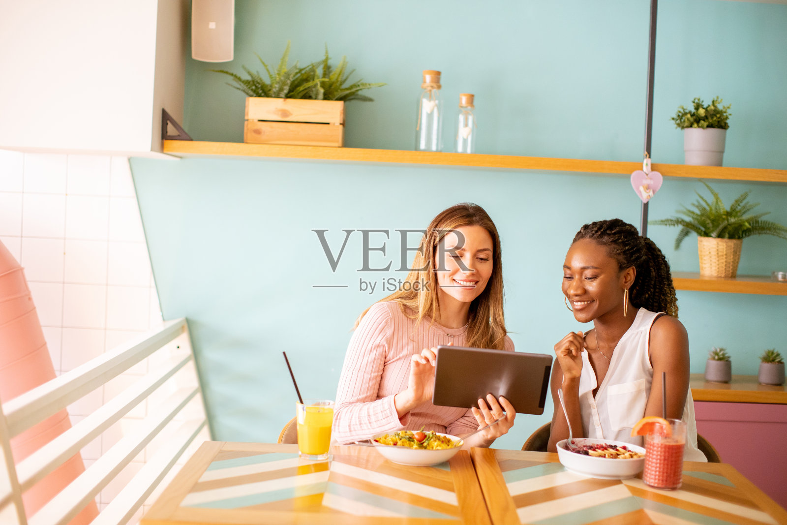 年轻的黑人和白人女性玩得很开心,喝着新鲜果汁,在咖啡馆吃着健康的早餐照片摄影图片