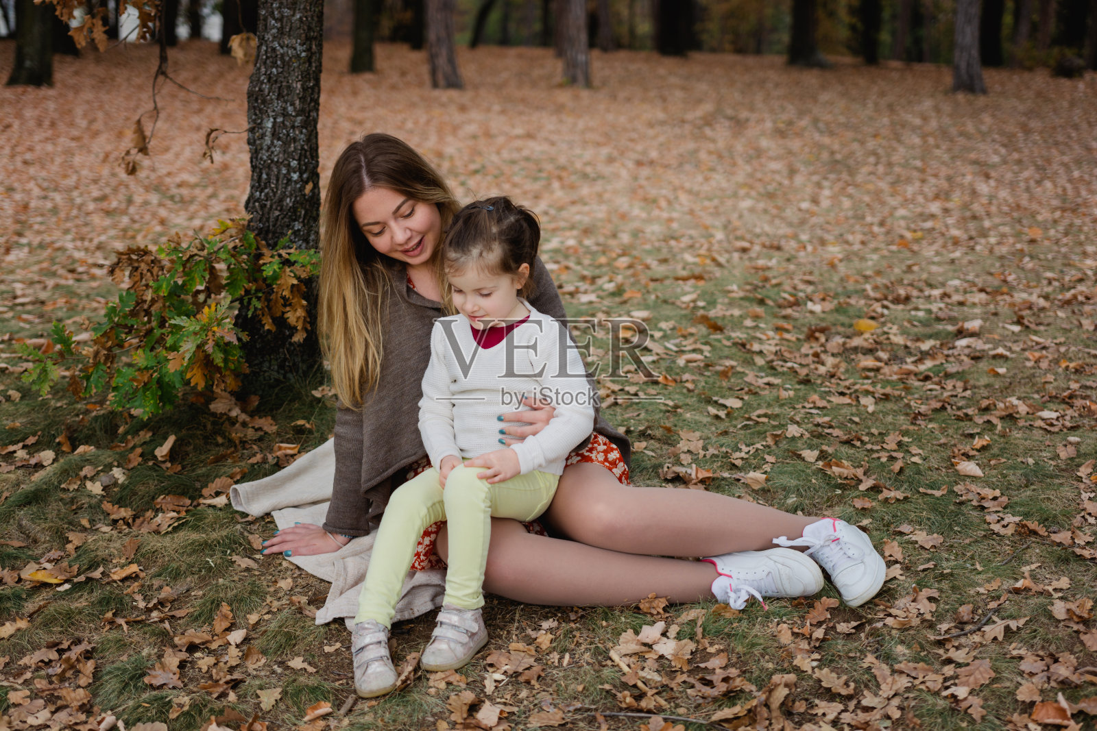 快乐的妈妈和女儿坐在秋天的公园里聊天照片摄影图片