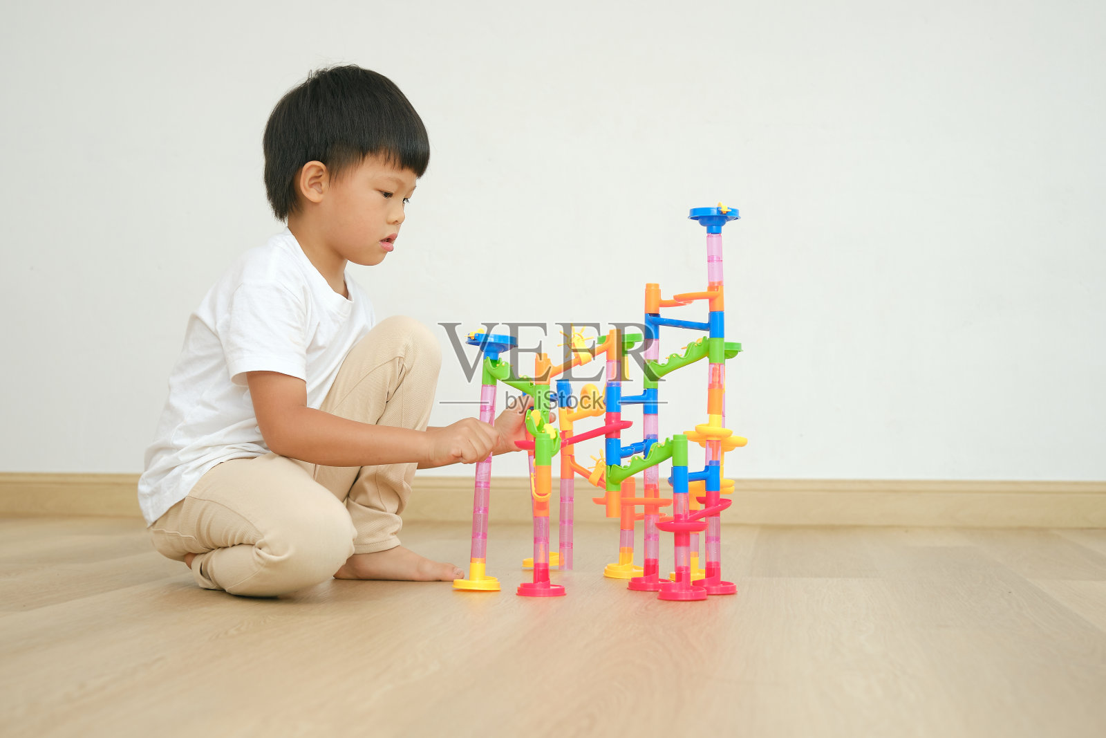 亚洲男孩坐在地板上玩彩色塑料大理石跑道玩具套装照片摄影图片