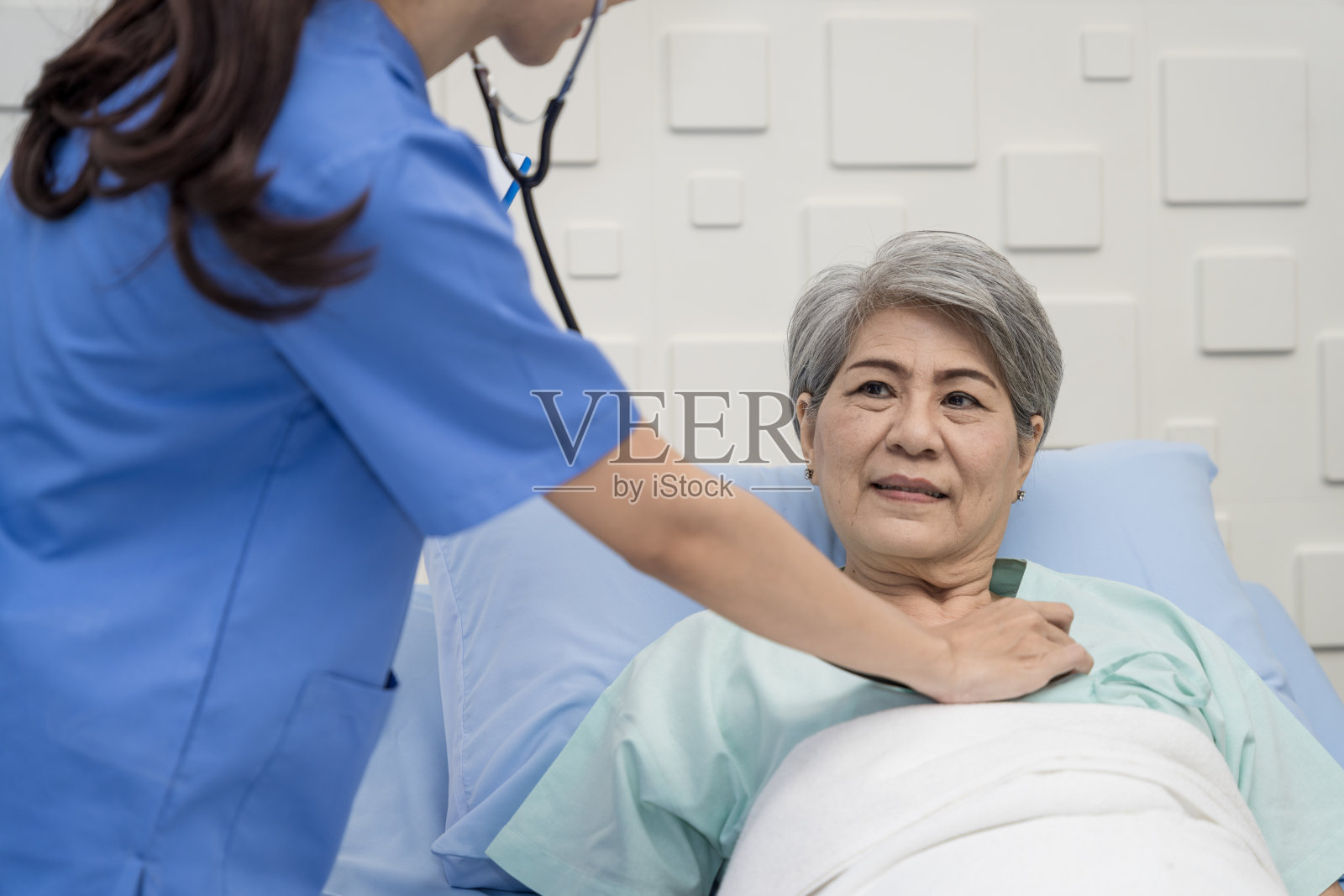 一名女护士或医生正在照顾一位躺在病床上做心脏和呼吸测试的老年女性患者。病人面带微笑照片摄影图片