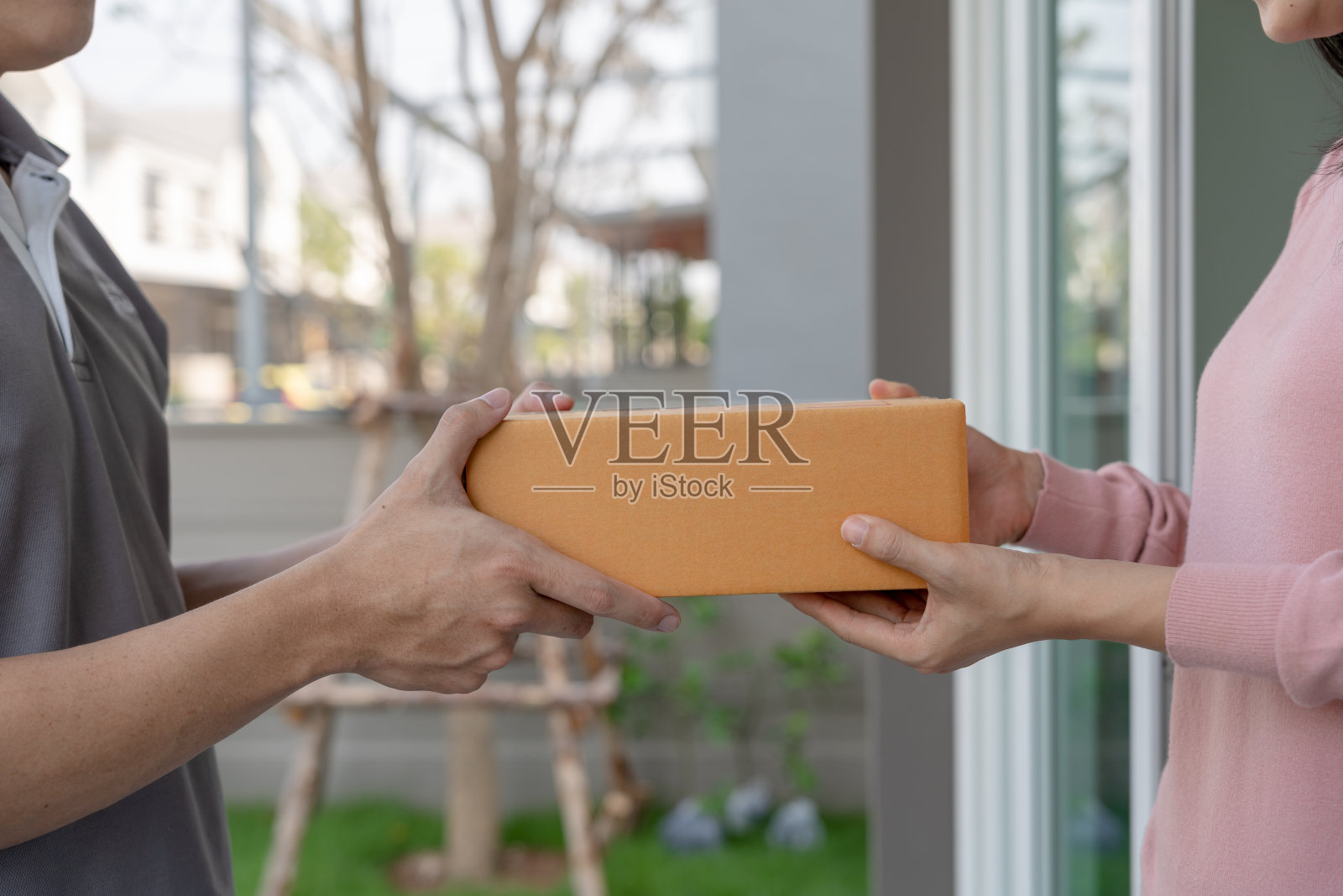 快乐的微笑女人收到盒子包裹从快递员在前面的房子。快递员送快递。网上购物,纸盒,外卖,邮递员,送货服务,包裹照片摄影图片