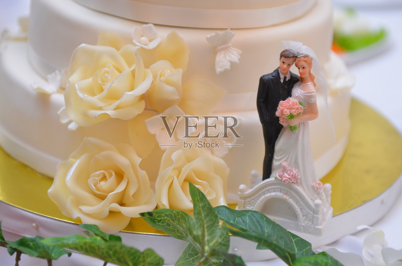 婚礼蛋糕,白色奶油和米色粉色玫瑰,新娘和新郎的雕塑在金支架上照片摄影图片