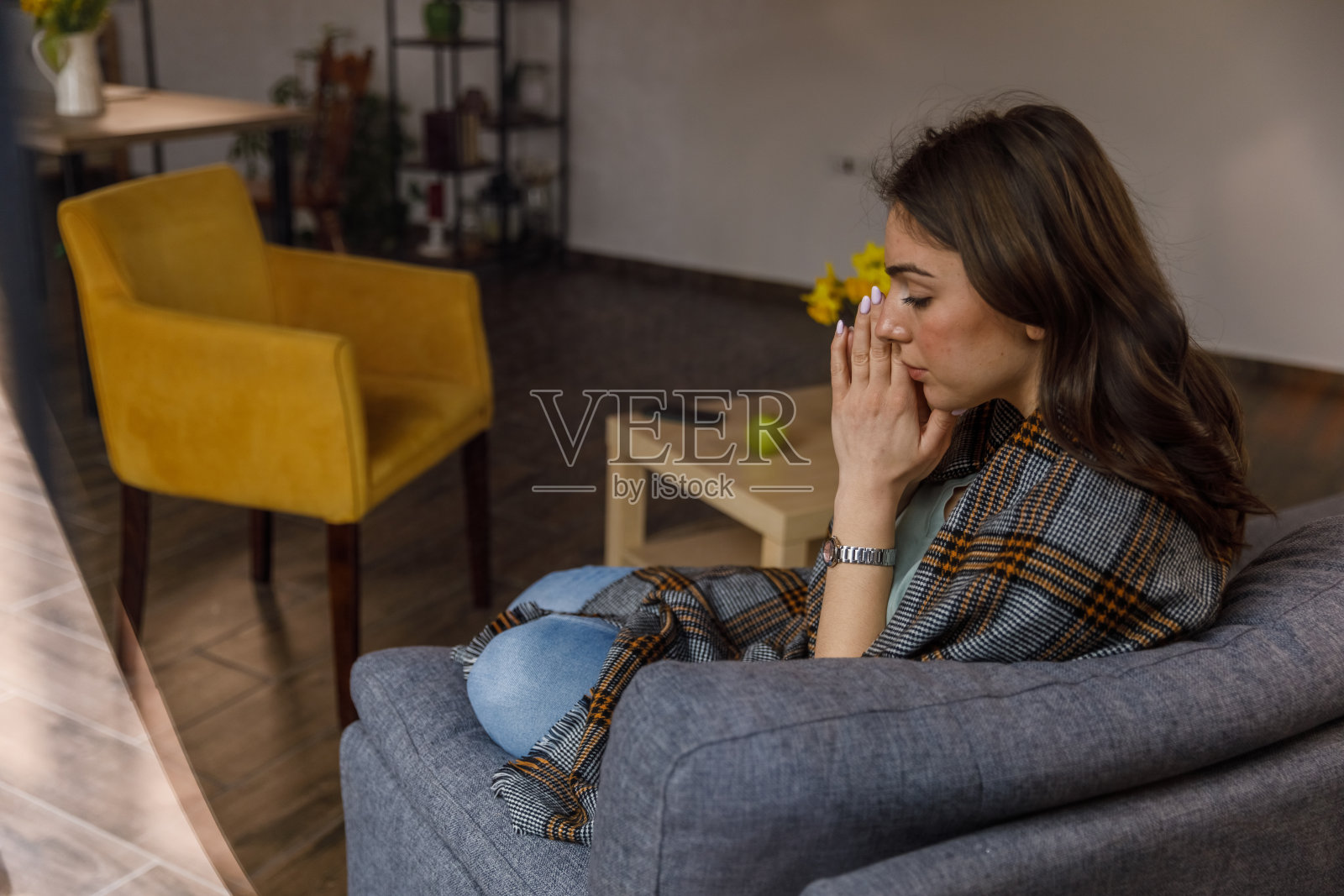 年轻的女人坐在沙发上,裹着毯子,坐立不安照片摄影图片