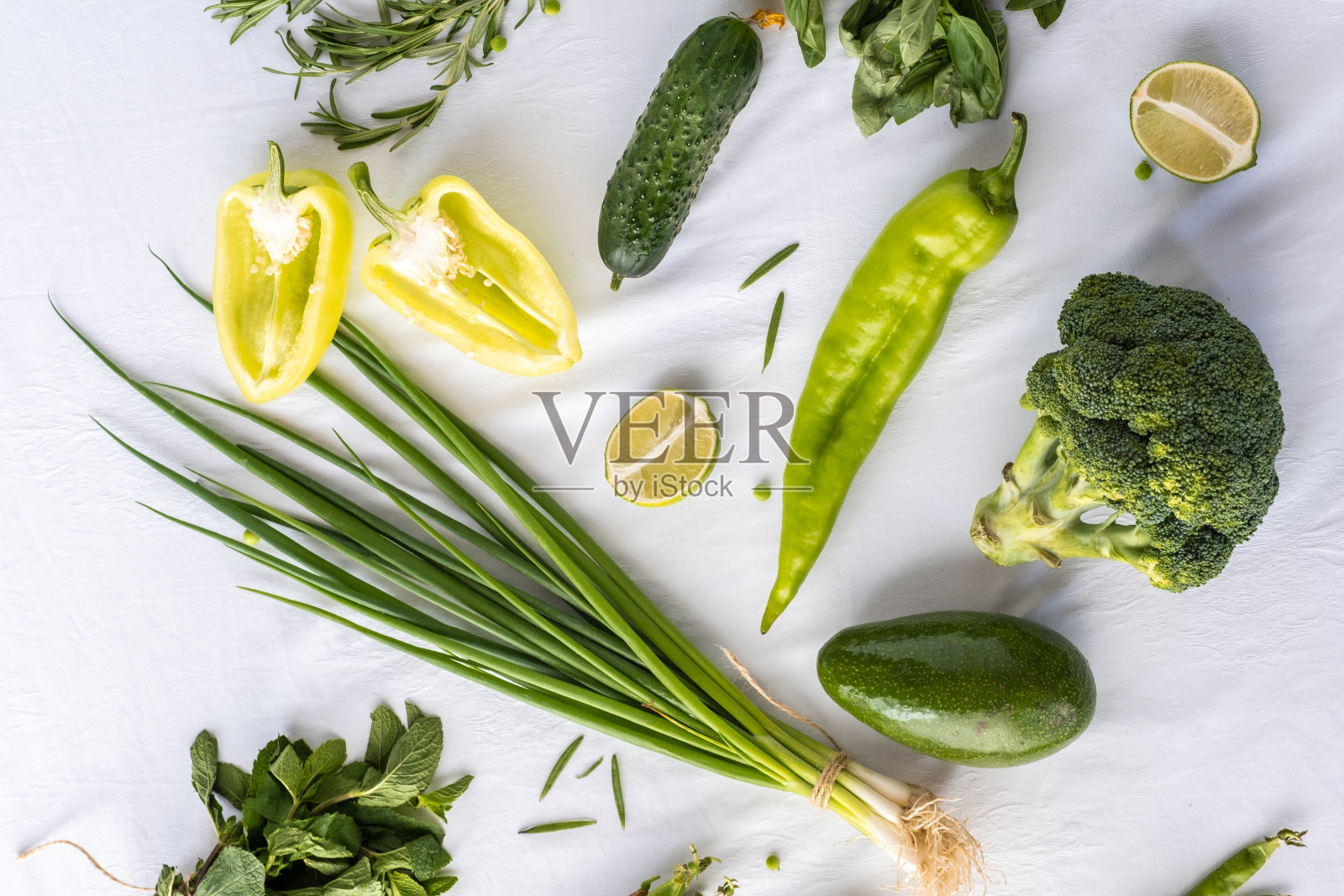 绿色的蔬菜放在白色的桌布上。洋葱,鳄梨,胡椒粉,柠檬,黄瓜。照片摄影图片