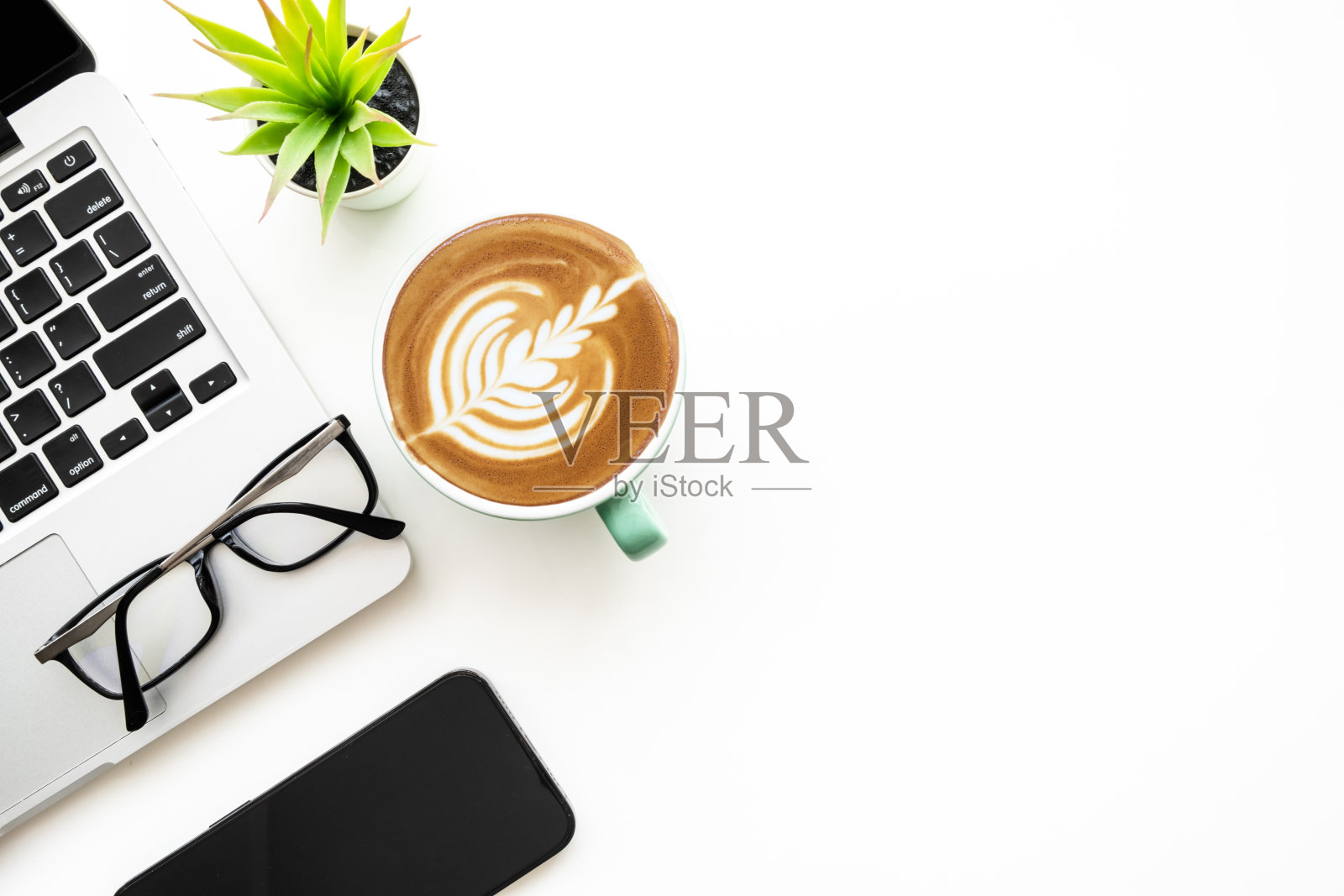 白色的办公桌,桌上有笔记本电脑,一杯热拿铁咖啡和办公用品。顶视图与复制空间,平铺。照片摄影图片