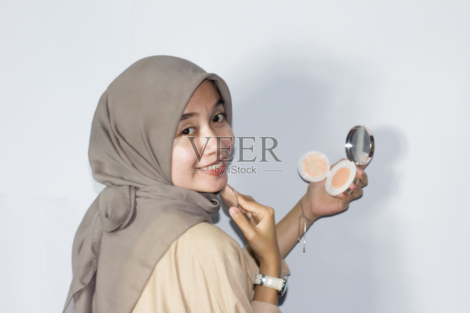 年轻的戴头巾的妇女拿着镜子在脸上化妆。孤立的背景照片摄影图片