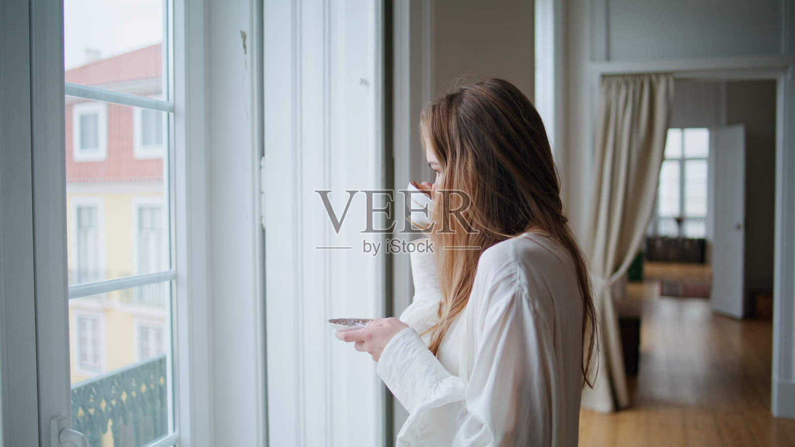 冷静的女人喝咖啡在平坦的内部特写。女孩看着橱窗摆姿势照片摄影图片