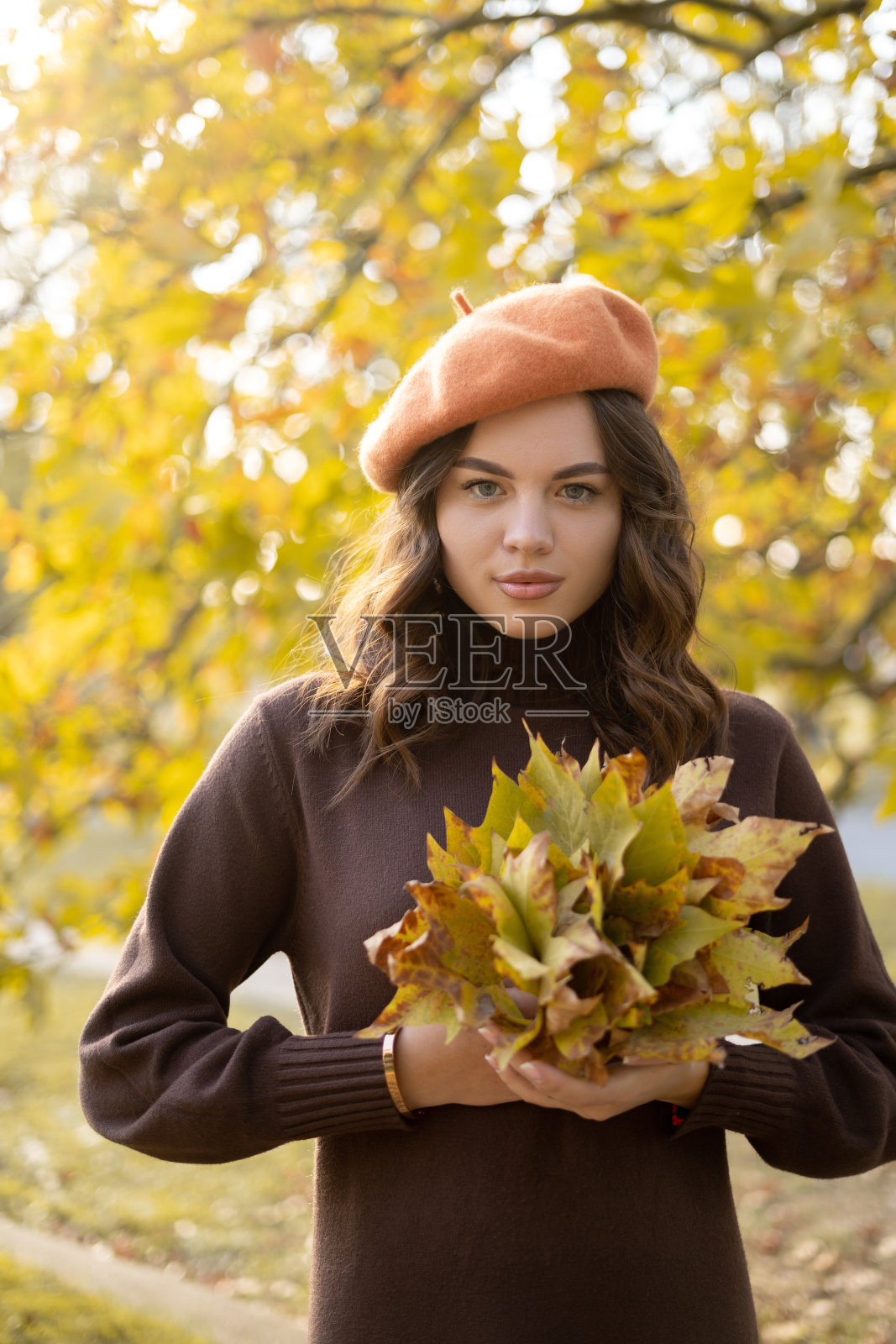 美丽快乐的年轻女子在公园里捧着秋天的树叶。开朗的女孩站在户外的秋天公园。充满活力的颜色。秋天的概念。照片摄影图片