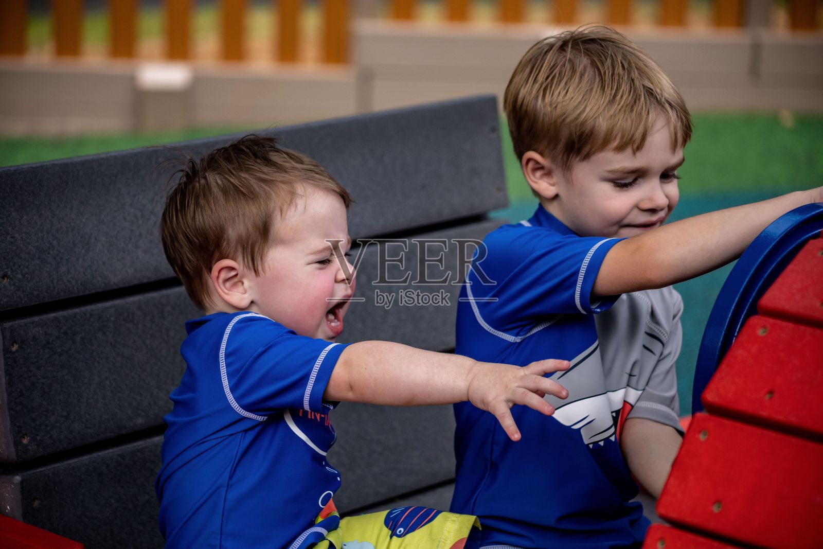 两个兄弟在操场上玩耍的特写,小男孩伸手哭泣,背景模糊照片摄影图片