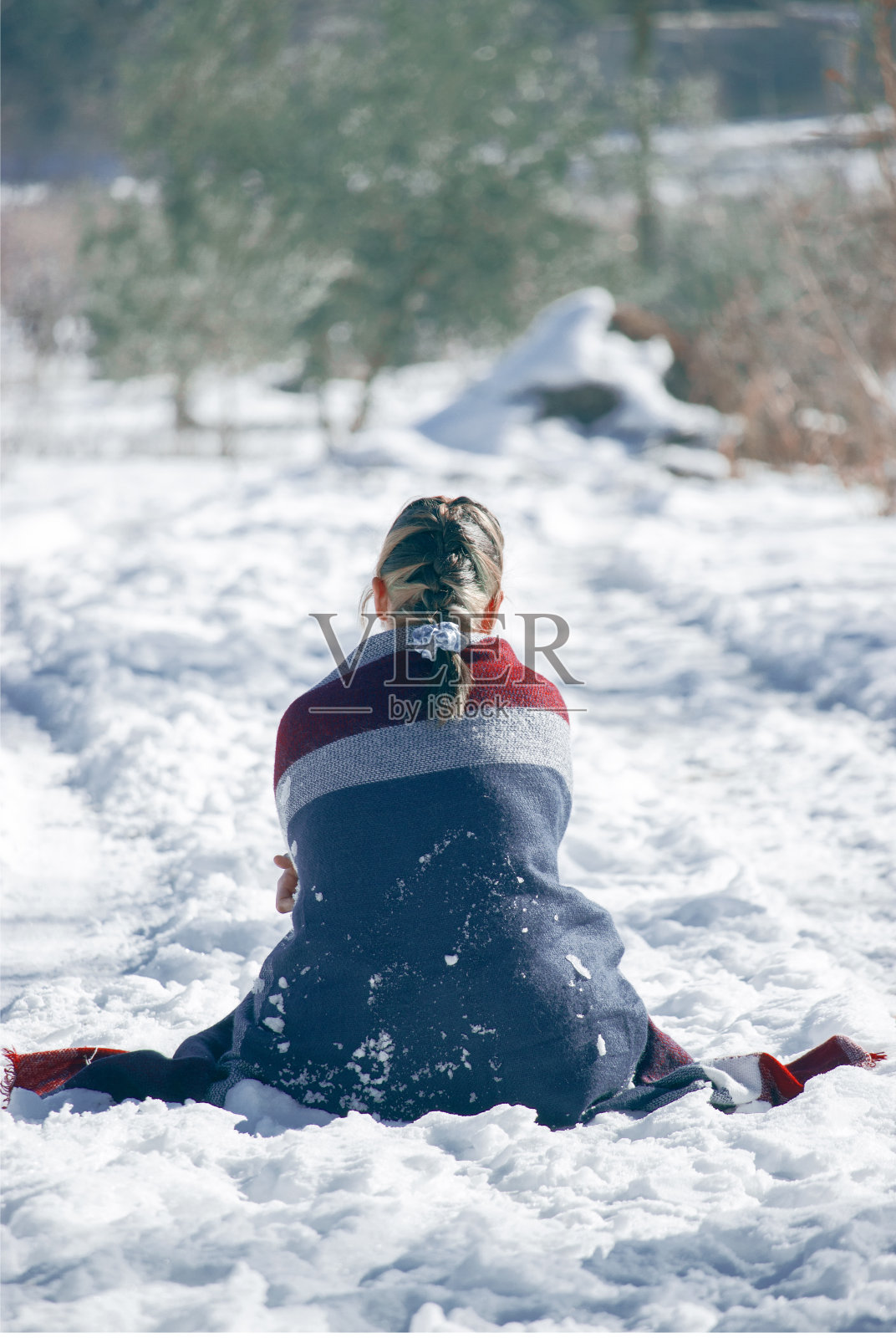 垂直选择性聚焦拍摄一位裹着冬季围巾的女士坐在雪地里照片摄影图片