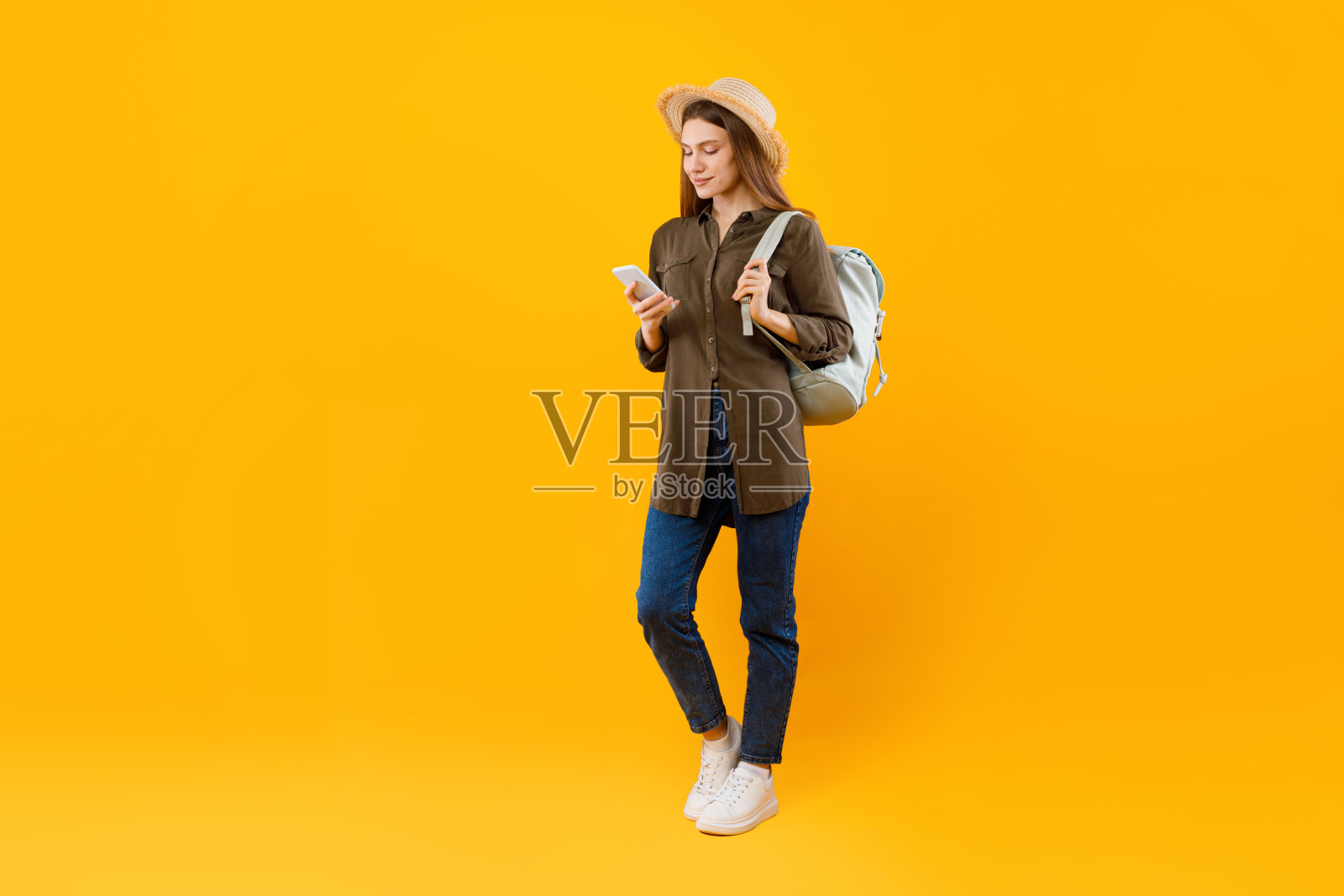 旅游女士用智能手机浏览互联网,背着背包,黄色背景照片摄影图片