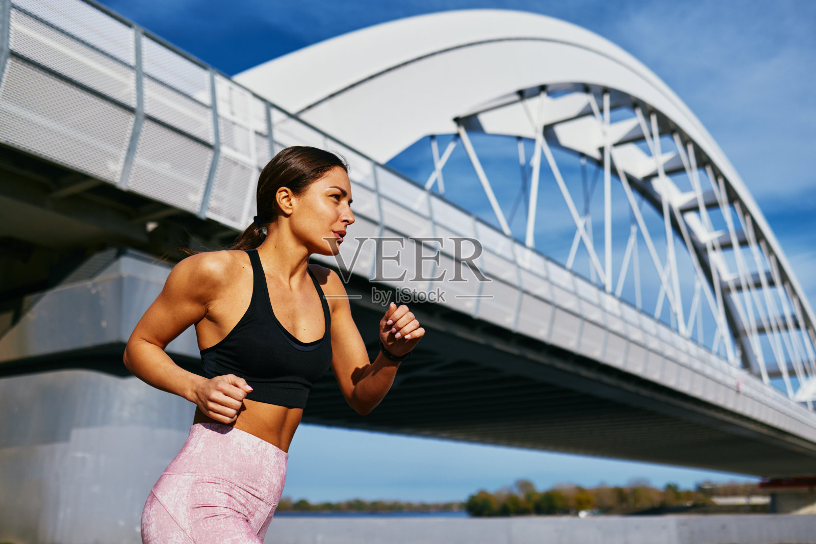 年轻的健身女子在河边和桥旁的小路上跑步照片摄影图片